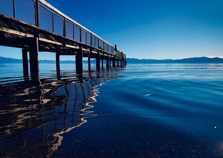 A wooden pier dock over blue, lakeside water, stretch out into the background distance..