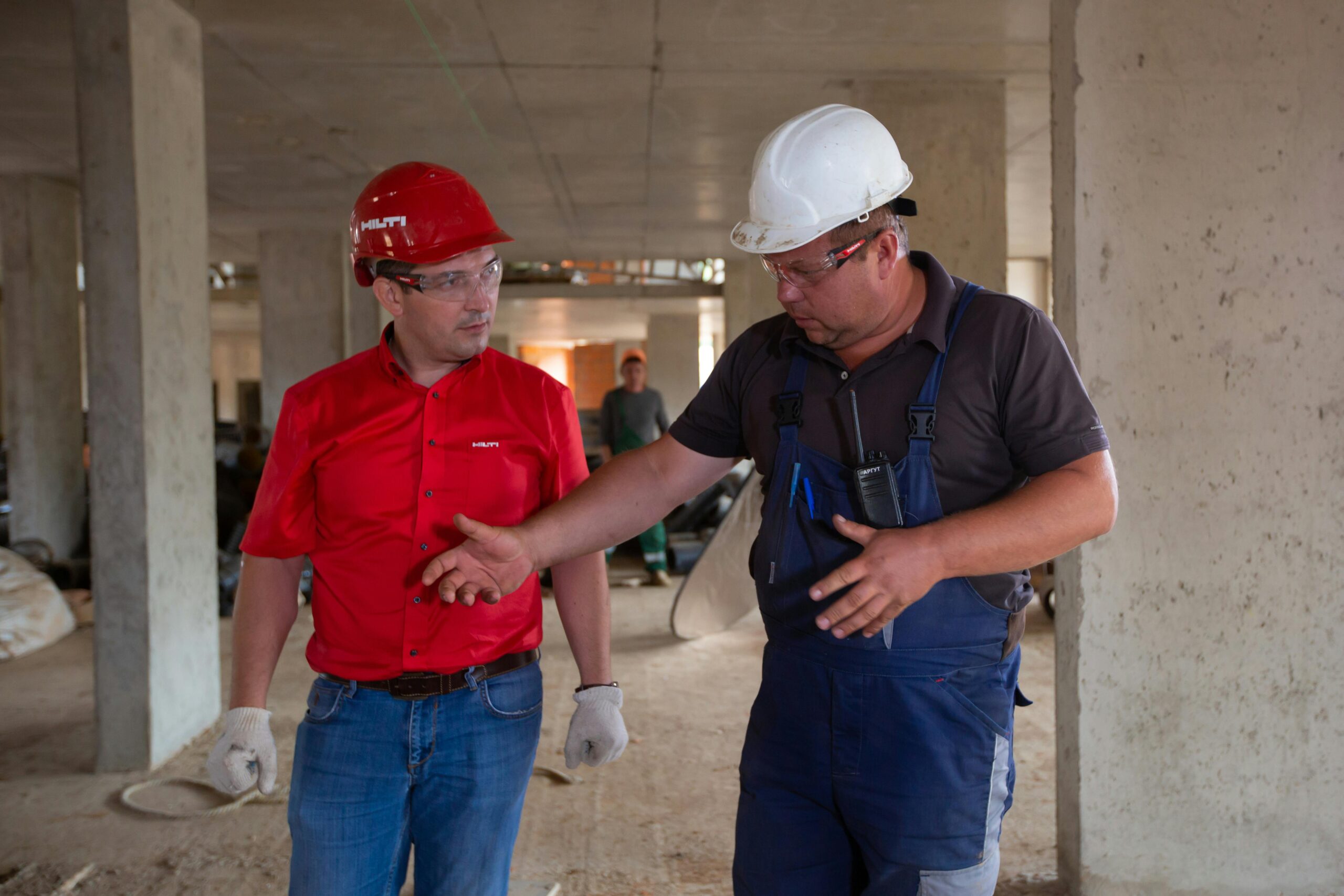 Two construction workers in safety gear discussing plans at a construction site.